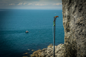 The Pongoose Climber 700 clipstick function; pole extended next to rock face with stunning blue sea and boat behind.